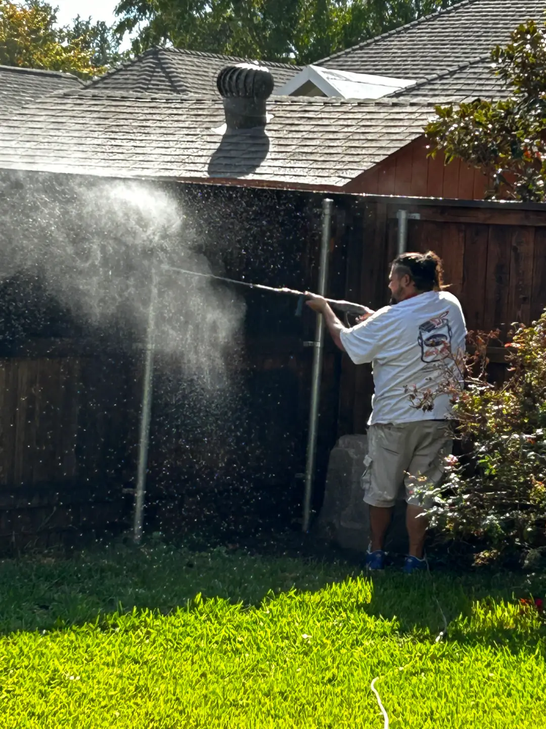 Crew member powerwashing an old wooden fence to strip stain and clean it before restaining