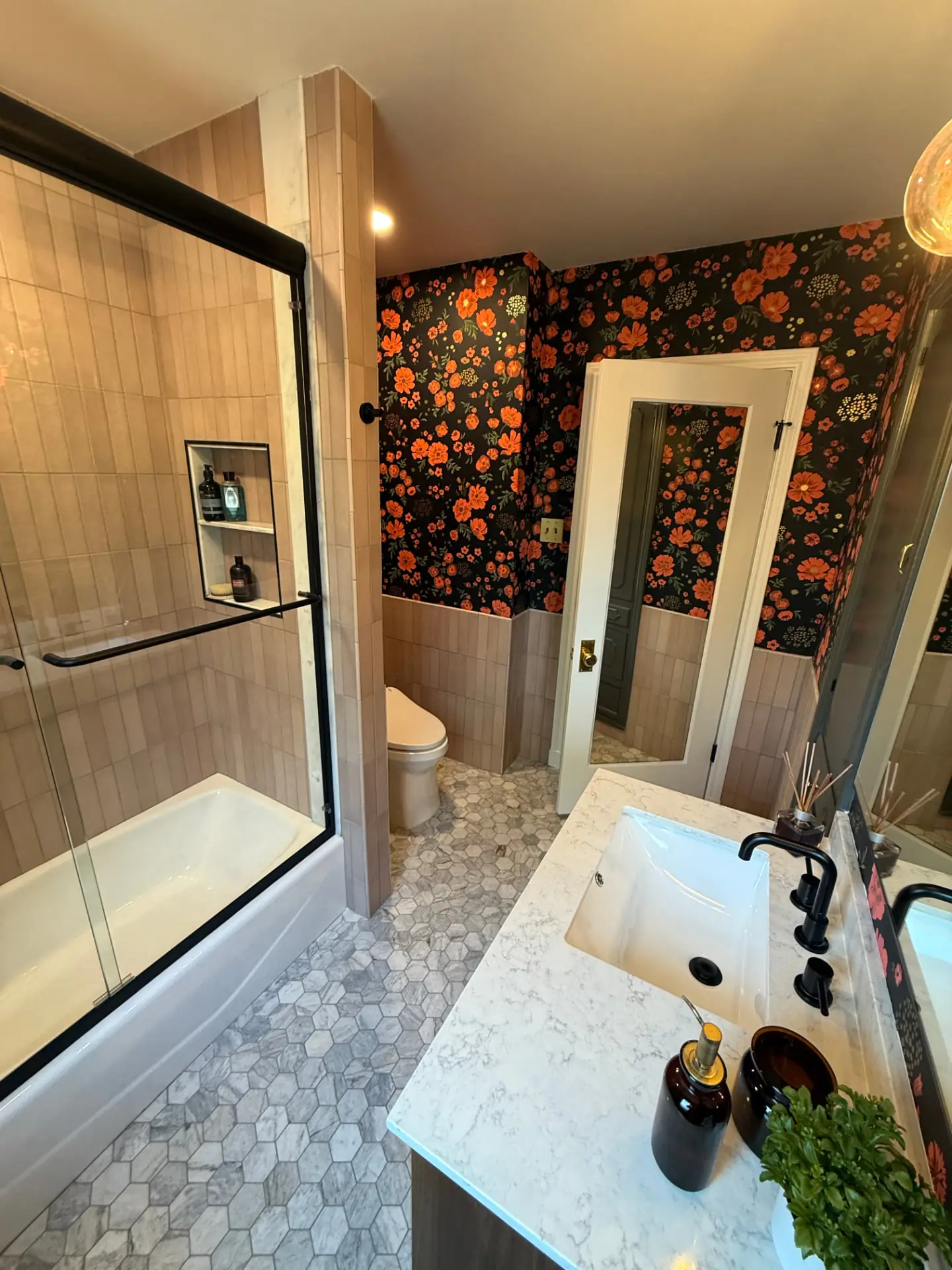 Bathroom vanity with an undermount sink and black fixtures beside a framed doorway, floral wallpaper, and hexagon floor tile