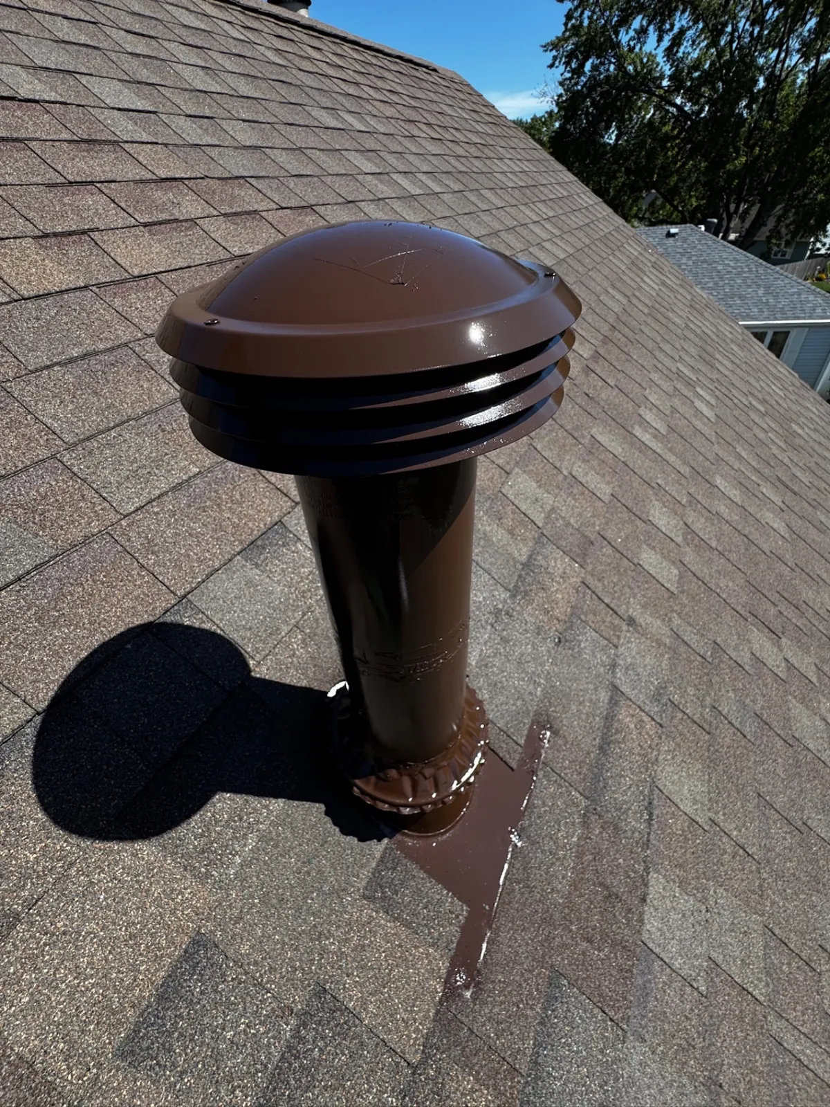 Vent stack freshly painted brown with sealed flashing on an asphalt shingle roof