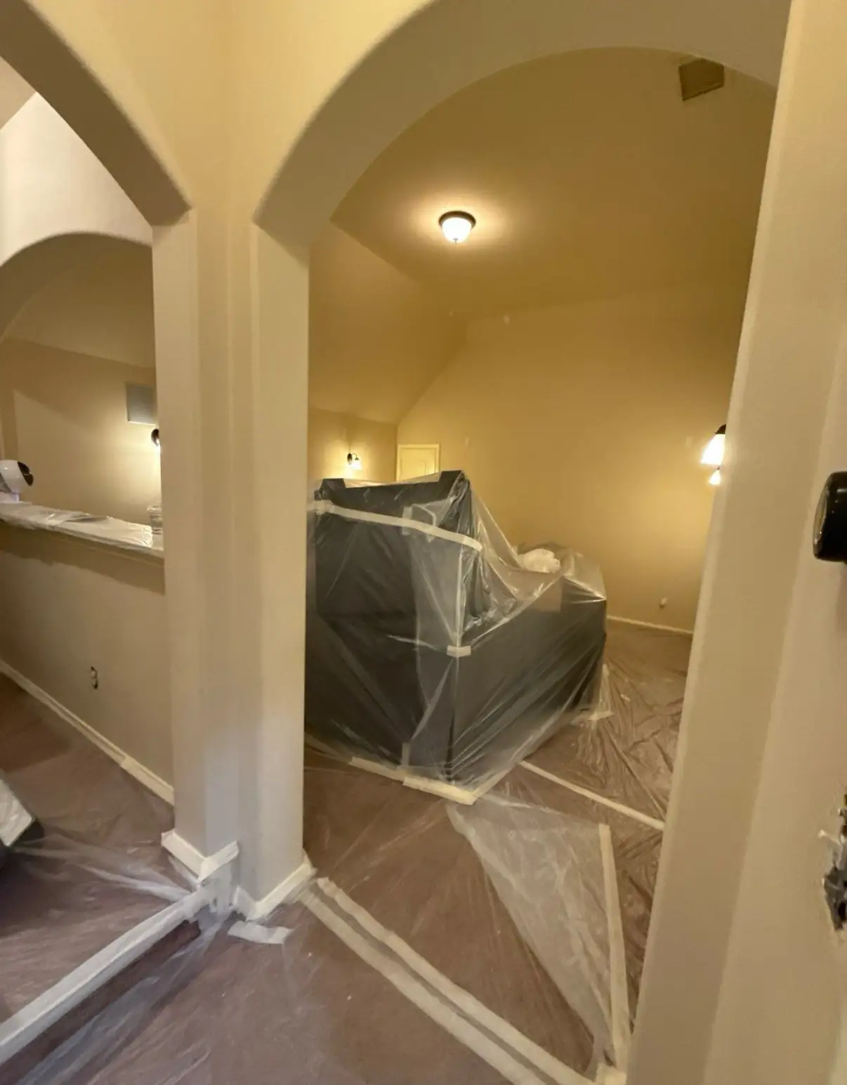 Furniture and floors covered in plastic sheeting inside a vaulted room being painted