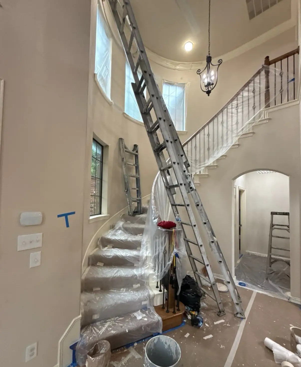 Curved staircase with railings and steps wrapped in protective plastic during an interior repaint