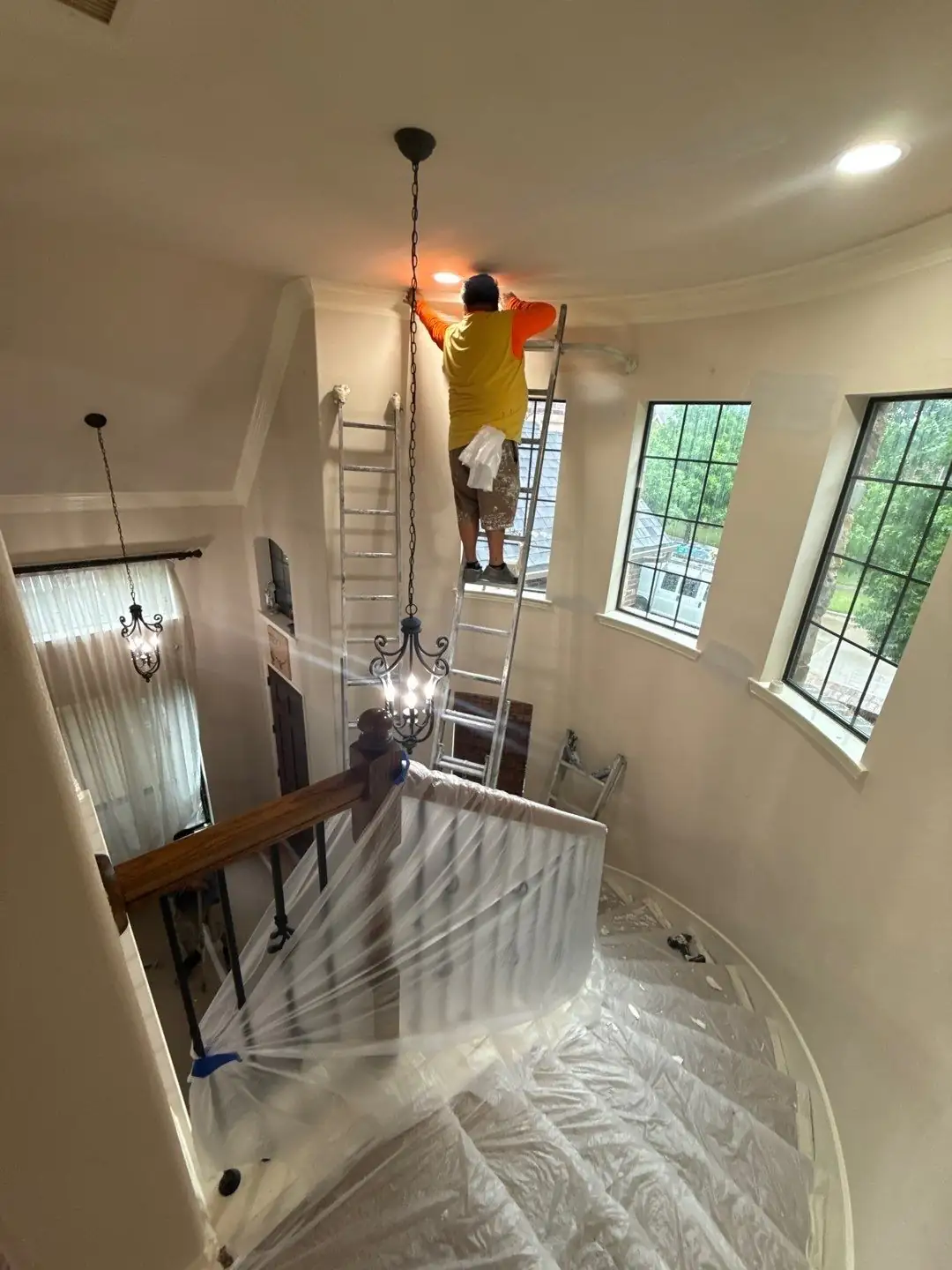 Painter on a ladder finishing crown molding and recessed lighting in a two-story curved foyer